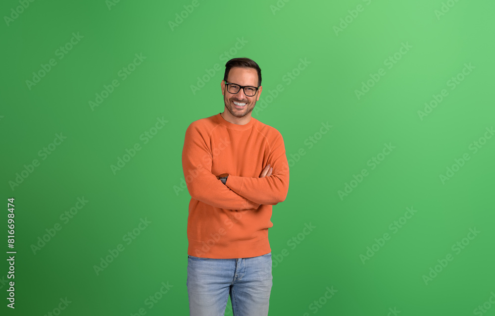 Young handsome entrepreneur standing with arms crossed and smiling at camera on green background Young handsome entrepreneur standing with arms crossed and smiling at camera on green background
