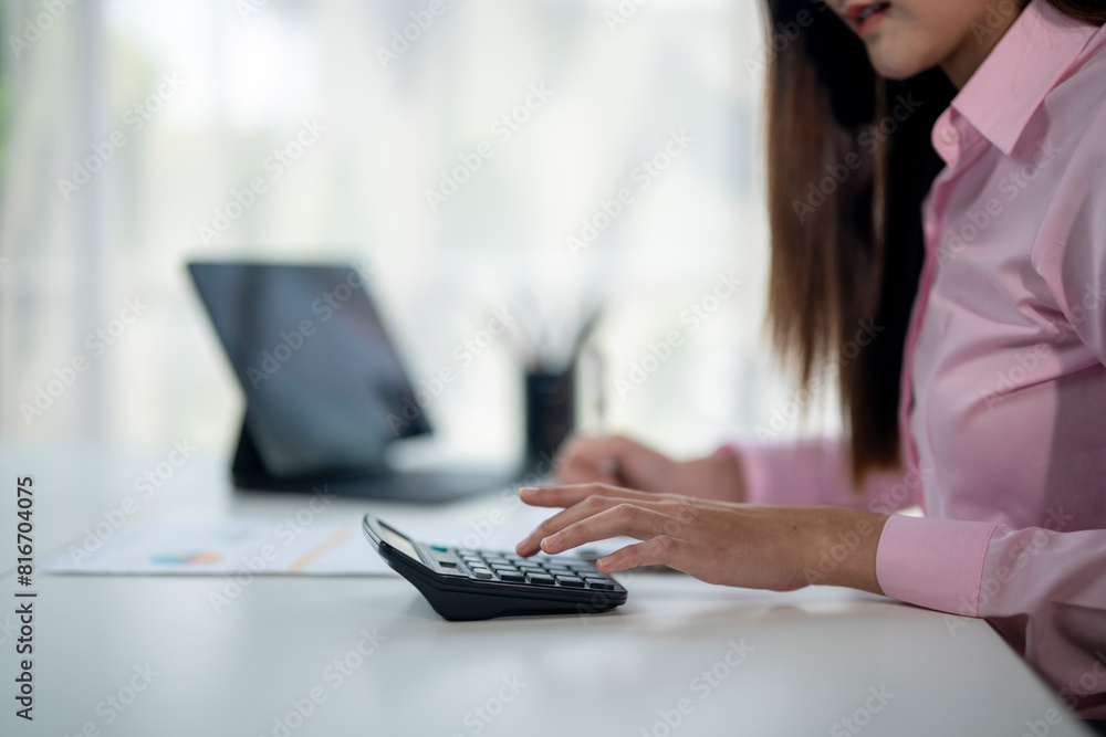 A woman is sitting at a desk with a calculator and a laptop A woman is sitting at a desk with a calculator and a laptop