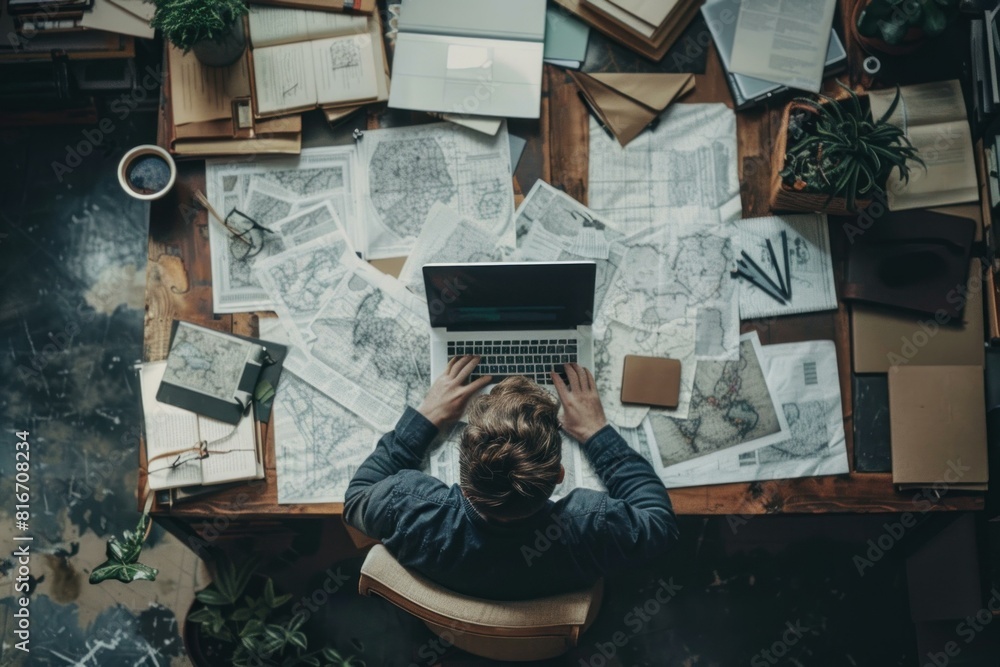 Overhead view of a person's workspace covered in maps and papers, planning a journey Overhead view of a person's workspace covered in maps and papers, planning a journey