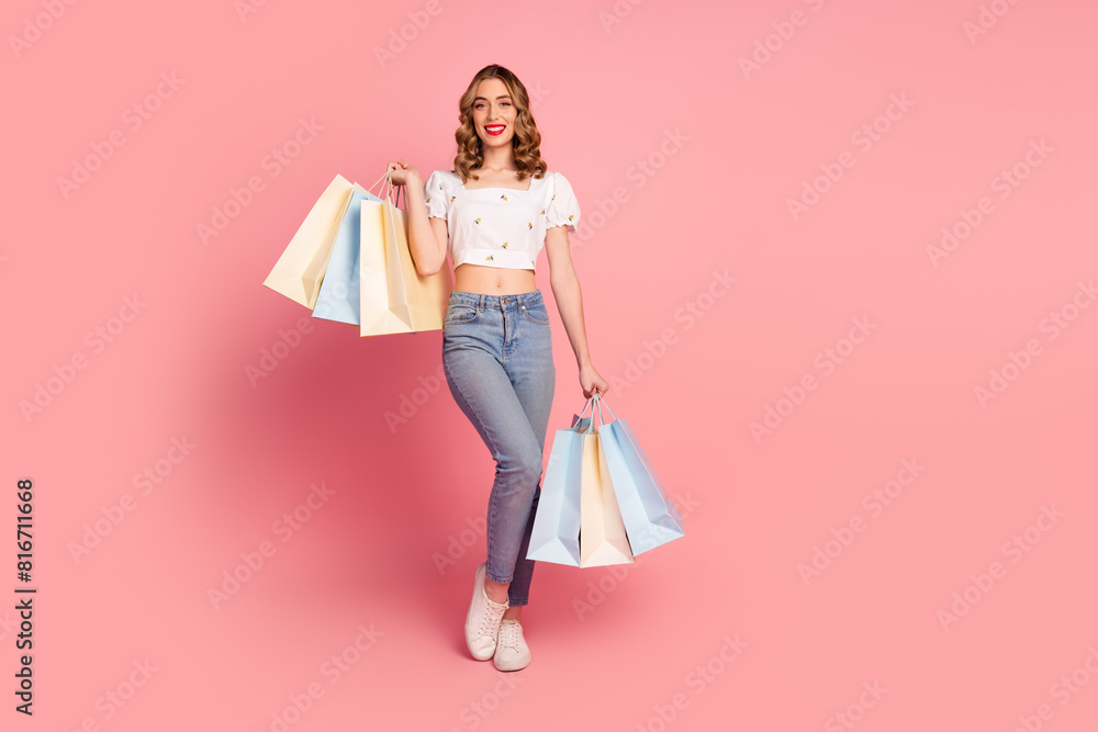 Full size photo of satisfied optimistic nice woman dressed white blouse jeans holding shopping bags isolated on pink color background Full size photo of satisfied optimistic nice woman dressed white blouse jeans holding shopping bags isolated on pink color background