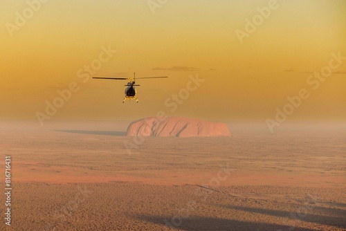 Helicopter flying over an expansive desert with Uluru in the background. Australia