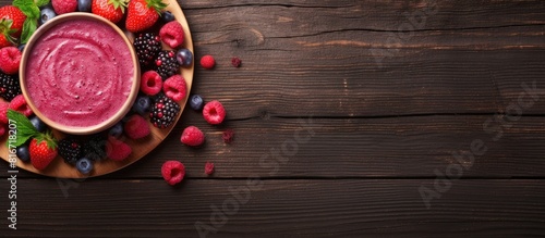 A top down view of a wooden table showcasing a bowl filled with raspberry smoothie and an assortment of berries leaving space to add text or images. with copy space image