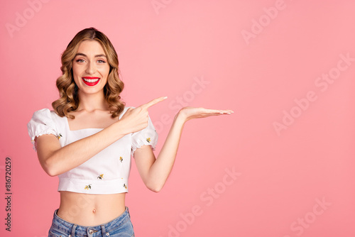 Photo portrait of pretty young girl point palm hold empty space wear trendy white outfit hairdo isolated on pink color background