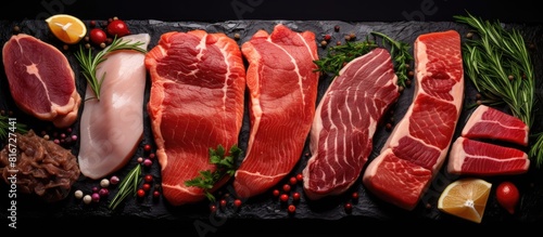 Copy space image of a top view of a variety of raw steaks including salmon beef pork and chicken placed on a black background