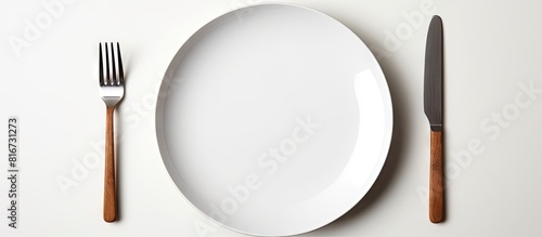 A white plate with a fork and knife placed on a white background leaving empty space for other elements in the image. with copy space image. Place for adding text or design