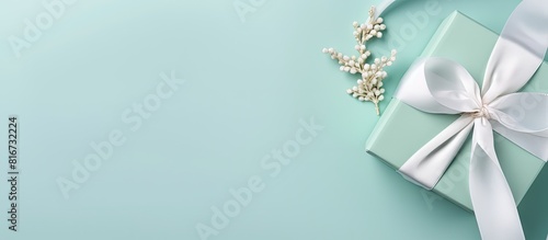 Copy space image of a top view flat lay featuring a white gift box adorned with a tiffany satin ribbon against a serene mint blue backdrop