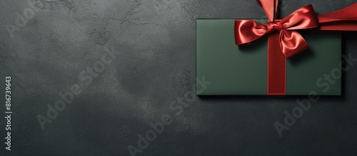 Top view of a dark green background with a blank gift card adorned with a red bow allowing space for text. with copy space image. Place for adding text or design © vxnaghiyev