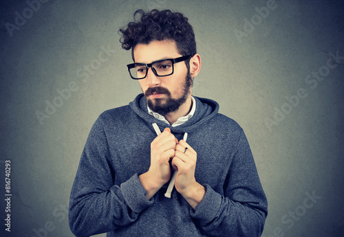 Lack of confidence. Shy anxious young handsome man feels awkward isolated on grey wall background.