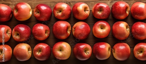 Fototapeta Naklejka Na Ścianę i Meble -  A wooden surface beneath showcases a top view of ripe red apples arranged in a grid like pattern The fresh fruits offer a copy space image