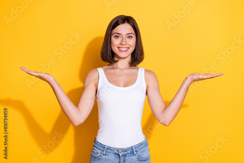 Photo portrait of attractive young girl compare hold empty space wear trendy white outfit isolated on yellow color background