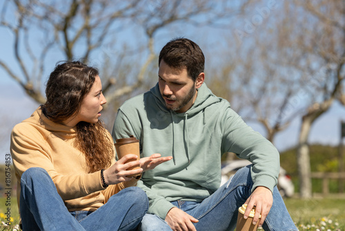couple in park arguing because they disagree. Young couple on a sunny day arguing about housework or work. Couple talking seriously outdoors in a park.