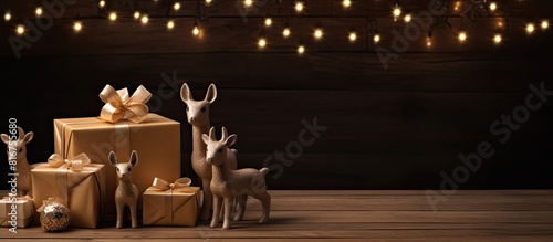 Tiny deer figurines holding a blank wish card by a toy Christmas tree and wrapped gift box against a dark wooden background Creative holidays season mockup. copy space available