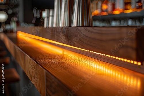 Closeup of undercabinet lighting fixtures installed beneath a wooden bar counter, illuminated with warm orange lights photo