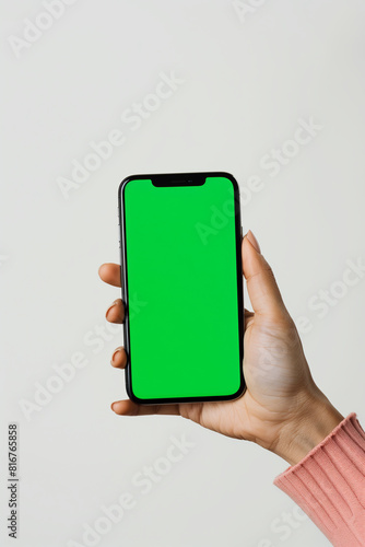 Female hand holding a smartphone with a blank green screen on solid white background.