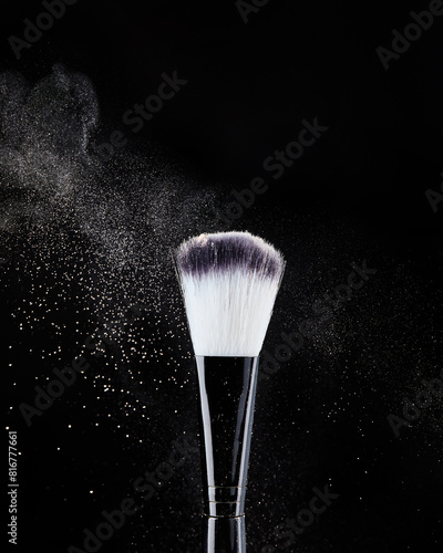 Professional black makeup brushes with beige powder in motion and loose powder particles scattered around in the form of cloud