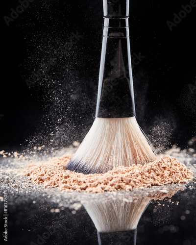 Makeup brush with loose cosmetic powder on black background.