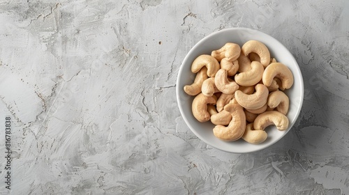 Cashew nuts in a white bowl on a textured background with their scientific name Anacardium occidentale and known as Kaju Badam in Bengali language Viewed from above photo