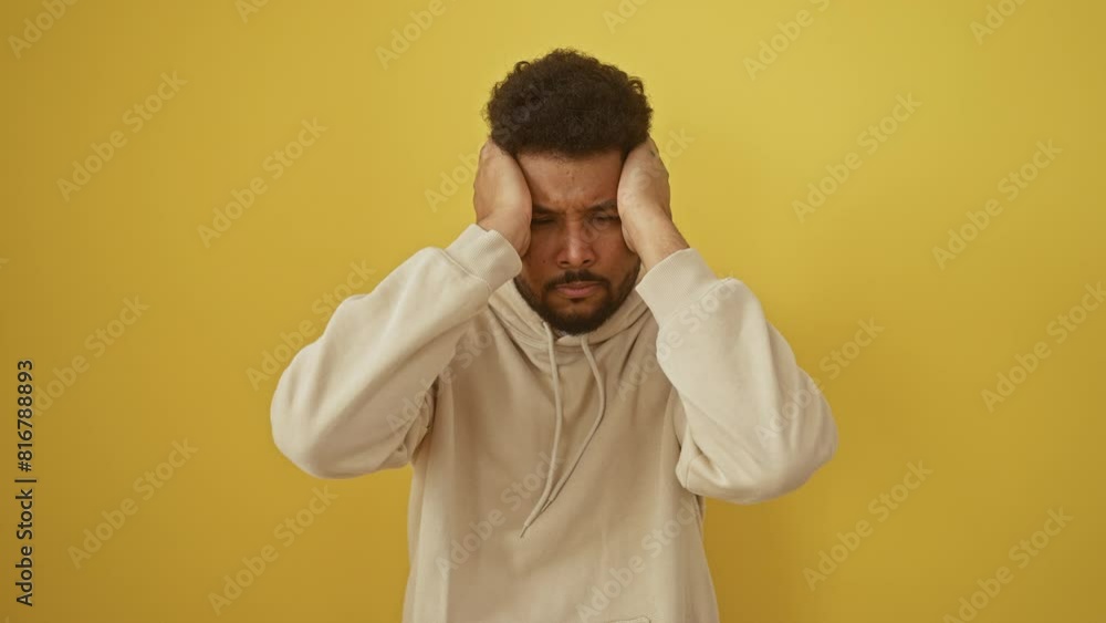 Desperate, stressed african american man, hands clutching head, suffering migraine pain. wearing hoodie, agonizing from headache against isolated yellow background. Desperate, stressed african american man, hands clutching head, suffering migraine pain. wearing hoodie, agonizing from headache against isolated yellow background.