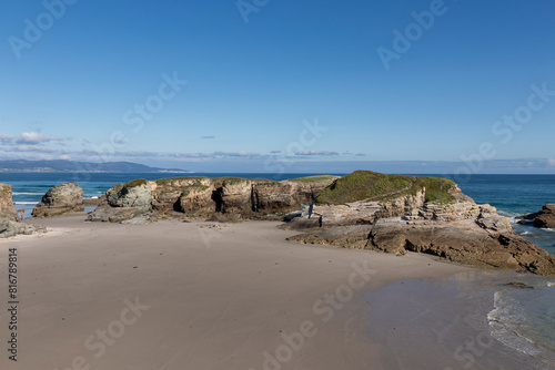 A serene beach with rocky formations, clear blue skies, and calm waters, evoking a sense of tranquility and natural beauty in asturias photo