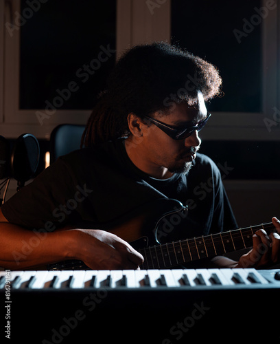 black african blind man musician playing guitar recording in production studio with piano