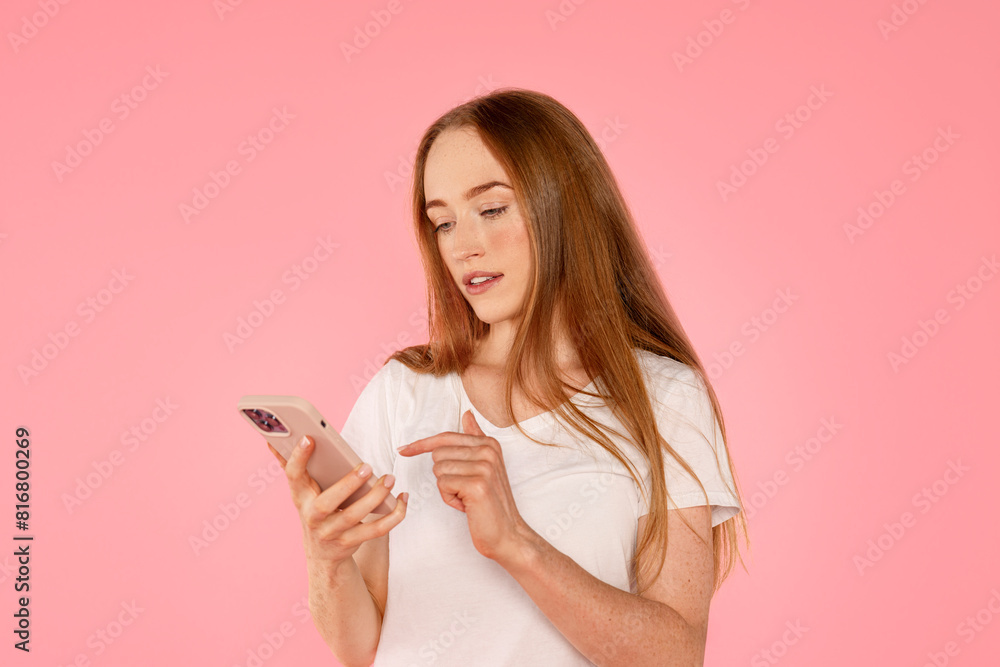 young redhead woman with freckles using mobile phone looking at smartphone typing message isolated on pink background young redhead woman with freckles using mobile phone looking at smartphone typing message isolated on pink background