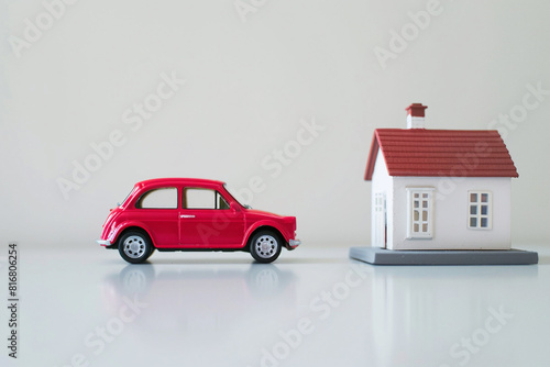 The concept of acquiring basic things to live in modern world. Red miniature car and white house on background stand on table.  © CozyDigital