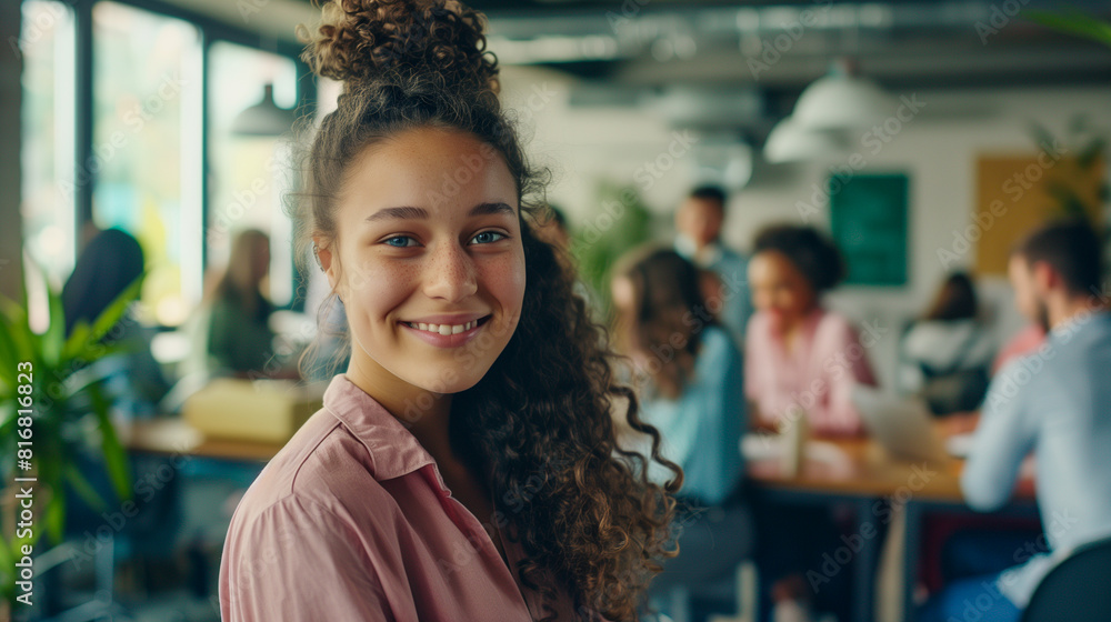 of pretty smiling girl standing in office looking at camera while people multi-ethnic team are working in background. Youth and business . of pretty smiling girl standing in office looking at camera while people multi-ethnic team are working in background. Youth and business .