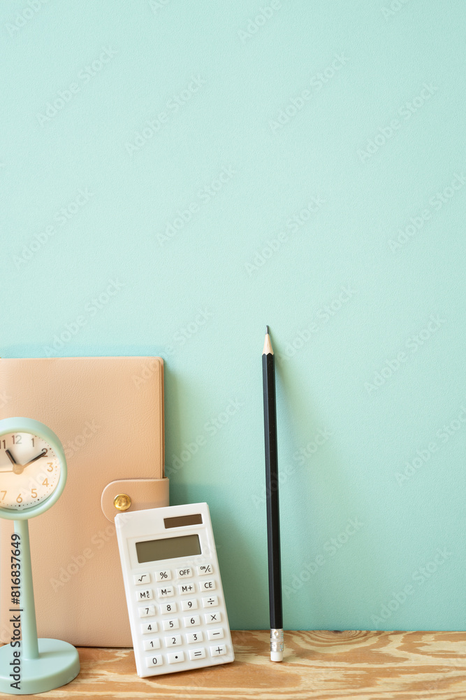 Workspace diary note, calculator, pencil, clock on wooden desk. mint wall background