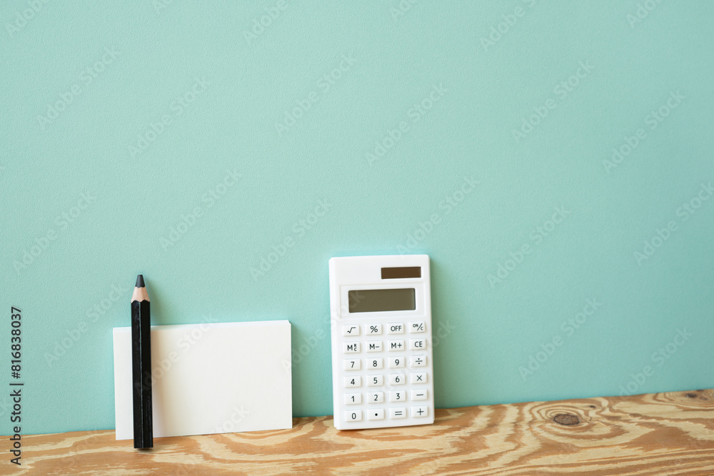 Calculator and memo pad, pencil on wooden desk. mint wall background
