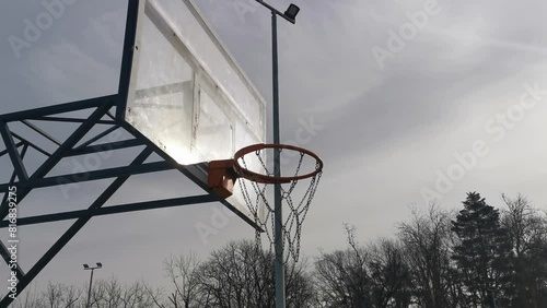 A basketball net under a cloudy sky. The back board has been busted and is now covered with a large piece of wood. photo