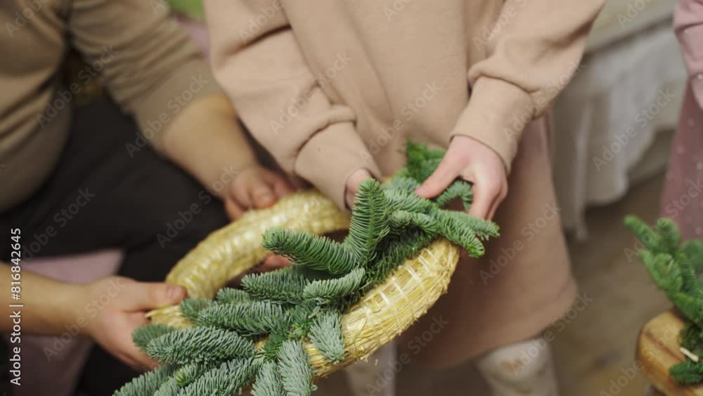 A girl skillfully adds pine needles to a wreath, creating a festive and traditional decoration for the holiday season. A girl skillfully adds pine needles to a wreath, creating a festive and traditional decoration for the holiday season.