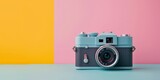 A blue vintage camera sits on a blue table against a pink and yellow background.
