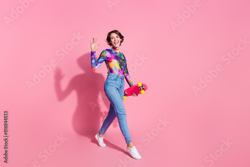 Full body portrait of pretty girl hold skate arm wave hi wear pullover isolated on pink color background © deagreez