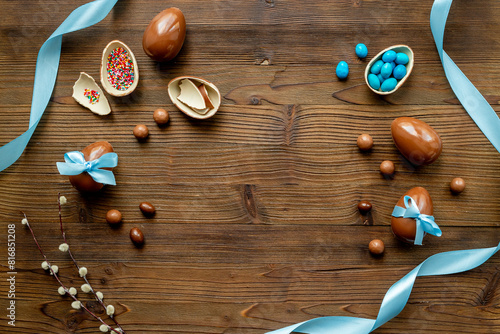 Chocolate Easter eggs in blue ribbon with sweets on brown wooden background