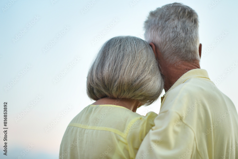 Happy elderly couple hugging against sky background Happy elderly couple hugging against sky background