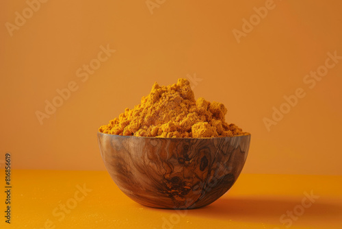 Wooden bowl overflowing with bright ground turmeric powder against a warm orange background, reflecting a sense of health and spice photo