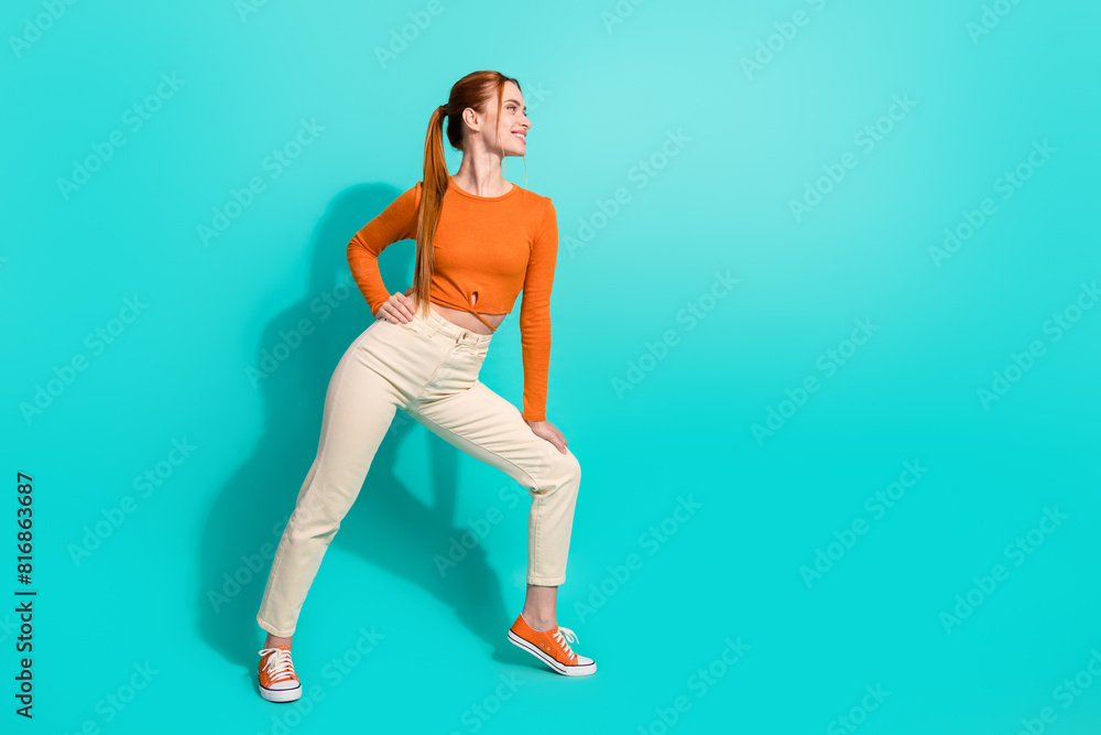Full size photo of positive girl with ginger hair dressed orange shirt look at promo empty space isolated on teal color background Full size photo of positive girl with ginger hair dressed orange shirt look at promo empty space isolated on teal color background
