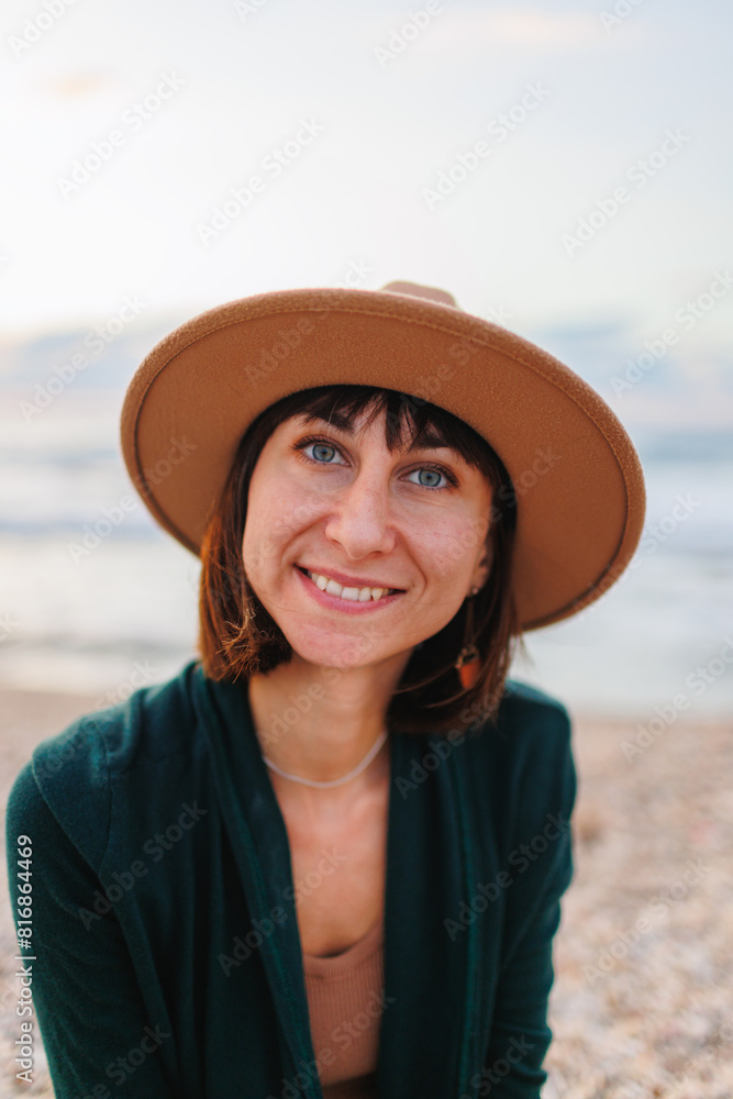 Portrait of a young smiling girl in a hat, sitting on the beach..Beautiful natural beauty woman smiling and laughing, posing for the camera on the beach.