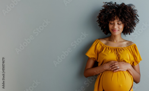 Pregnant African American woman tenderly hugging her belly on a gray background. The concept of preparing women for pregnancy, childbirth, motherhood.