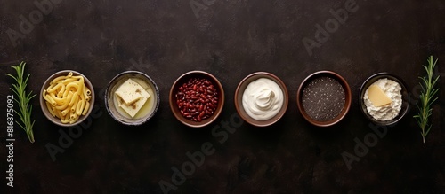Row of ceramic bowls with various kitchen ingredients, spices, pasta, sauces, legumes on dark background, banner 