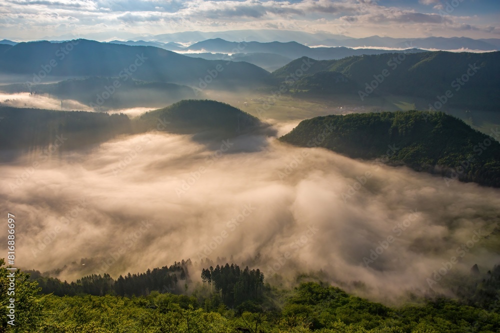 Rocky, forested hill emerges from the valley in the mist. Beautiful morning in the mountain landscape with mists. Morning fog. Sulovske skaly, Velky Manin Povazie Rocky, forested hill emerges from the valley in the mist. Beautiful morning in the mountain landscape with mists. Morning fog. Sulovske skaly, Velky Manin Povazie