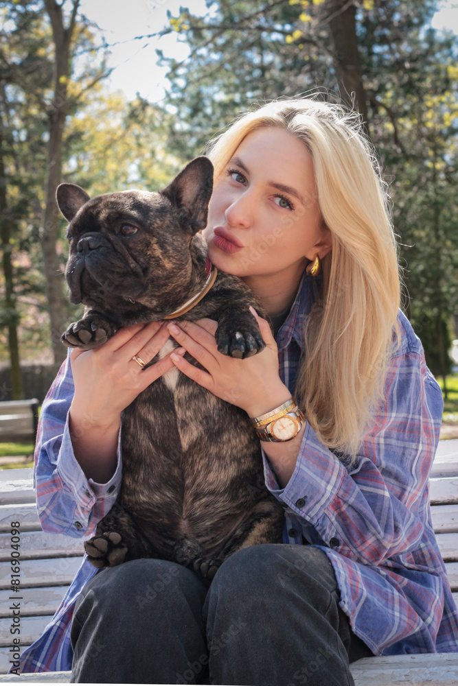 Beautiful girl with blonde hair walking with her pet, French bulldog Beautiful girl with blonde hair walking with her pet, French bulldog