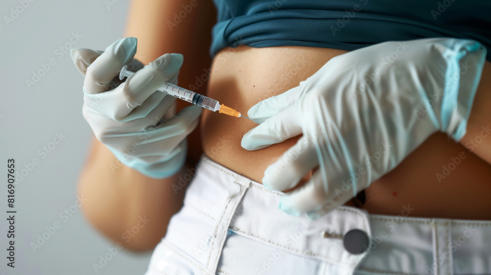 A person wearing medical gloves prepares to administer an injection into their abdomen area, indicating self-administration of medication or insulin. A person wearing medical gloves prepares to administer an injection into their abdomen area, indicating self-administration of medication or insulin.