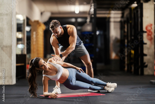 Personal trainer is helping a sportswoman with side planks in a gym.