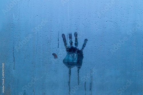 Palm print on foggy glass with water drops. Background is deep blue and gives gloomy impression