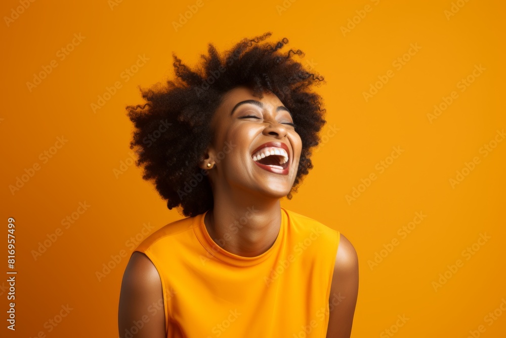 Portrait of a blissful afro-american woman in her 40s laughing while standing against soft orange background Portrait of a blissful afro-american woman in her 40s laughing while standing against soft orange background