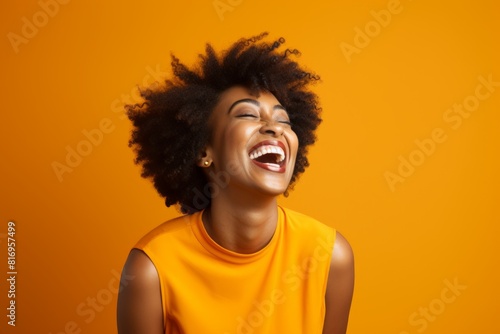 Portrait of a blissful afro-american woman in her 40s laughing while standing against soft orange background