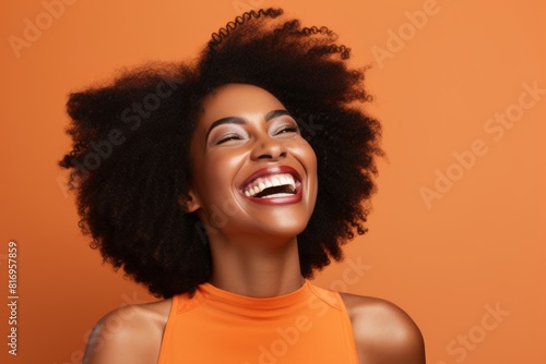 Portrait of a blissful afro-american woman in her 40s laughing over soft orange background