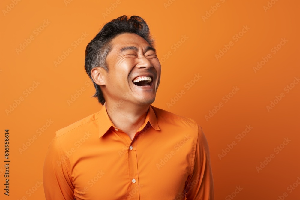Obraz premium Portrait of a glad asian man in his 40s laughing in soft orange background