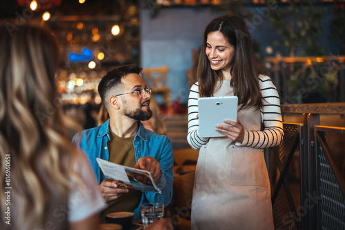 Foto A smiling waitress takes an order from guests at a cozy bar, with one man holding a menu and engaging in lively banter dressed in casual attire